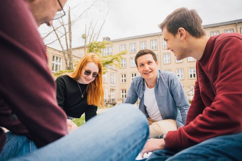 Studierende sitzen auf einer Wiese im Kreis.