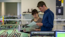 Praktikum im Eisenbahnlabor; zwei Studierende vor der Eisenbahnanlage studieren die Aufgabenstellung