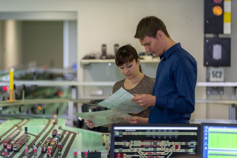 Praktikum im Eisenbahnlabor; zwei Studierende vor der Eisenbahnanlage studieren die Aufgabenstellung
