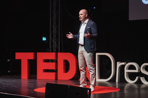 Prof. Dr. Lars Hornuf auf der TEDx Bühne, im Hintergrund der TEDx Dresden Schriftzug