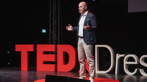 Prof. Dr. Lars Hornuf auf der TEDx Bühne, im Hintergrund der TEDx Dresden Schriftzug