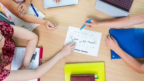 Studenten in Workshoprunde, Studenten sitzen an einem Tisch, man sieht nur ihre Hände, in der Mitte liegt ein Blatt Papier zu dem sie diskutieren