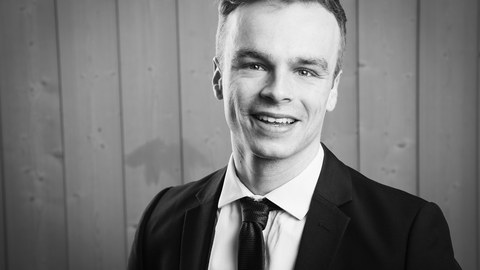 Schwarz-Weiß-Fotografie eines Mannes. Er lächelt. 