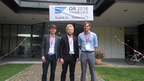 3 Männer in Anzügen vor einem Gebäude. 