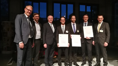 Gruppenbild: Preisträger mit Urkunden und Verantwortliche tragen Anzüge.
