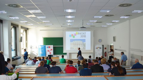 Lecture hall with several people in the rows of chairs. 