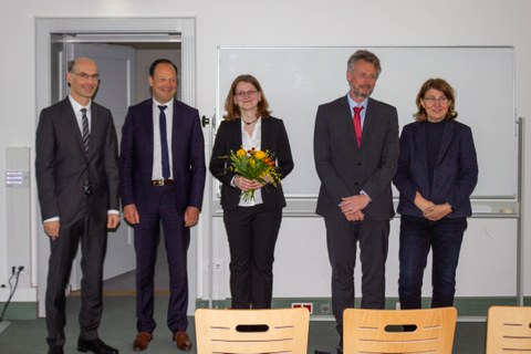 5 Personen in förmlicher Kleidung. Die Frau in der Mitte hält einen Blumenstrauß in der Hand.
