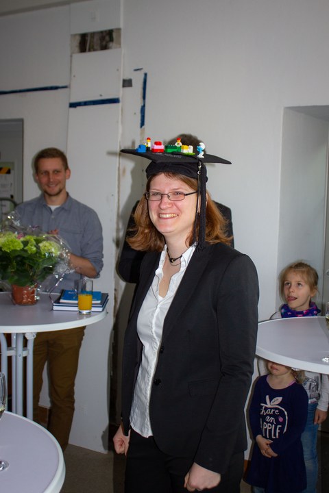 Eine Frau lächelt und trägt einen Doktorhut.