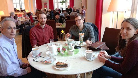 4 Personen sitzen an einem runden Tisch in einem Café.