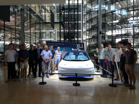 Groups of people stand around a white car. 