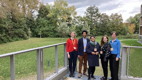 Team members of the junior professorship stand smiling in the greenery in front of the event building
