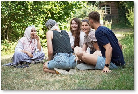 Es sind lachende Studierende zu sehen, die auf einer Wiese sitzen