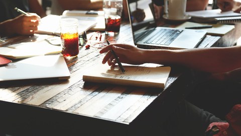 Man sieht einen Tisch, auf dem Notizbücher liegen und Getränke stehen