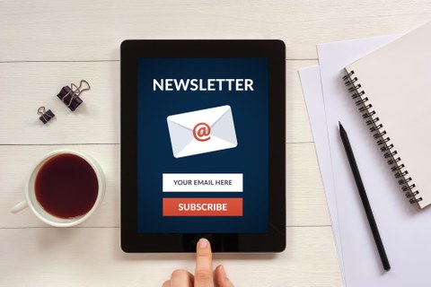 Zu sehen ist ein Tablett mit geöffneten Newsletter und eine Tasse Kaffee
