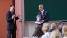 Zu sehen sind der Dekan und Prof. Rollberg. Prof. Rollberg hält ein Geschenk in den Händen und der Dekan bedankt sich bei ihm für seinen Vortrag 