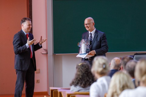 Zu sehen sind der Dekan und Prof. Rollberg. Prof. Rollberg hält ein Geschenk in den Händen und der Dekan bedankt sich bei ihm für seinen Vortrag 
