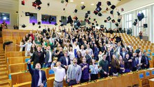Die Absolvent:innen werfen ihre Graduiertenhüte in die Luft für das bekannte Hutwerffoto. 