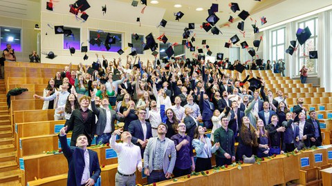Die Absolvent:innen werfen ihre Graduiertenhüte in die Luft für das bekannte Hutwerffoto. 