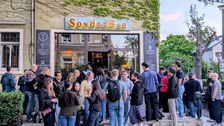 Zu sehen sind viele junge Menschen vor einer Bar.