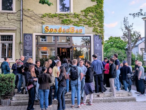 Zu sehen sind viele junge Menschen vor einer Bar.