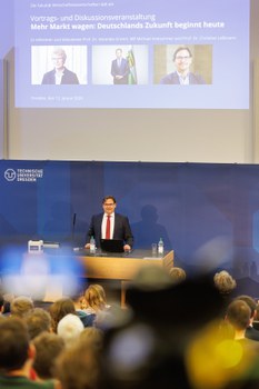 Man sieht Prof. Leßmann, der das Publikum begrüßt.