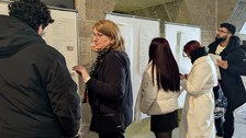 Zu sehen ist eine Professorin und Studieninteressierte, die sich an Infowänden unterhalten bzw. informieren. 