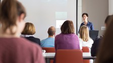 Das Foto zeigt eine Frau bei einer Präsentation vor vielen Personen