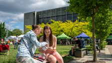 Foto von Mutter und Tochter, die draußen auf der Bank sitzen und Infomaterial durchschauen am Uni-tag 2022