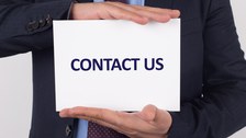 Das Foto zeigt eine Person im Anzug. Sie hält ein weißes Kärtchen zwischen den Händen. Auf diesem befindet sich die Aufschrift "CONTACT US"