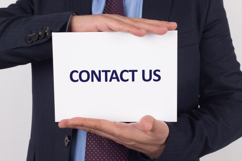 Das Foto zeigt eine Person im Anzug. Sie hält ein weißes Kärtchen zwischen den Händen. Auf diesem befindet sich die Aufschrift "CONTACT US"