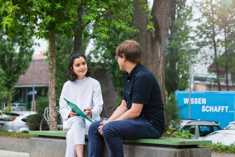 Ein Mann und eine Frau lernen zusammen und sitzen auf einer Bank im Park des Hörsaalzentrums.