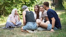 Foto von 5 Personen, die auf einer Wiese auf dem Campus der TU Dresden sitzen und sich unterhalten.