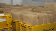 Das Foto zeigt viele gelbe Postkisten voller unzähliger brauner Briefe.