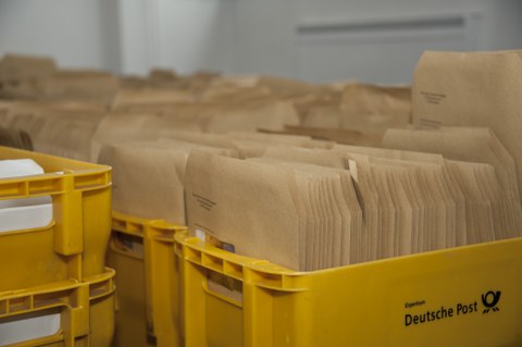 Das Foto zeigt viele gelbe Postkisten voller unzähliger brauner Briefe.