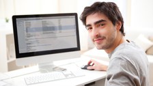 Foto: Ein junger Mann arbeitet an seinem Computer. Er lächelt und sieht glücklich aus.