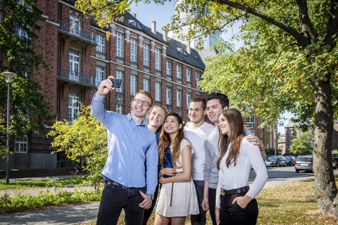  Eine Gruppe lächelnder Studenten macht vor einem TU Gebäude ein Gruppenfoto von sich.