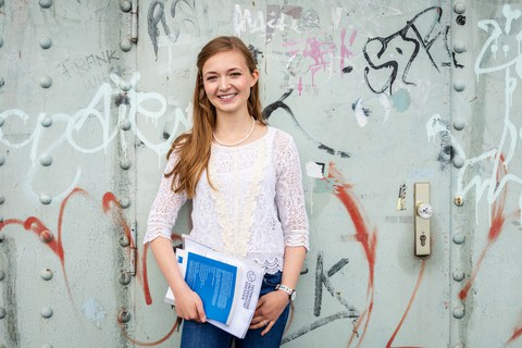 Foto: Eine Studentin der TUD steht lächelnd vor einer Metalltür mit Graffitis am Blauen Wunder.