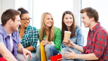 Das Foto zeigt fünf Studierende, die sich im Kreis gegenüber sitzen. Sie haben Hefter und Kaffeebecher in der Hand und lachen.