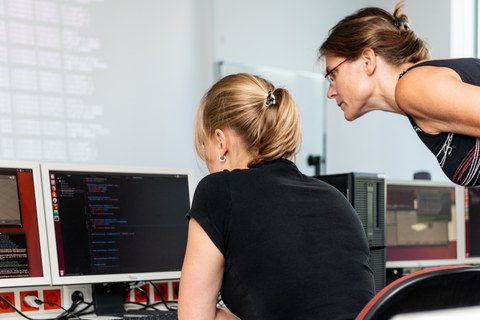 Foto: Eine Studentin und eine Dozentin beugen sich über einen Monitor in einem Computerkabinett