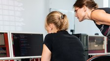 Foto: Eine Studentin und eine Dozentin beugen sich über einen Monitor in einem Computerkabinett