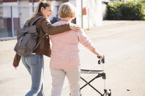 Foto zeigt eine ältere Frau, die mit ihrer Tochter an der Seite mit einem Rollator spazieren geht.