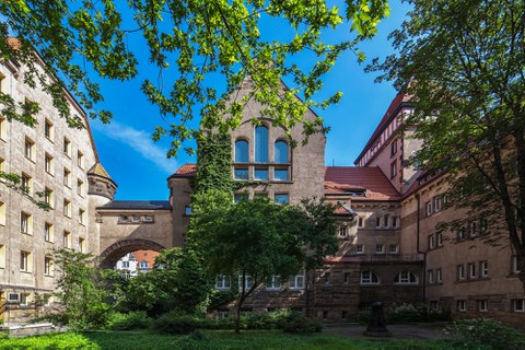 Innenhof des Tillich-Baus der TU Dresden. Dieser ist mit vielen Pflanzen und Bäumen bewachsen. Im Hintergrund erkennt man einen Torbogen.