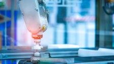 Foto eines Laufbands eines technischen Produktionsprozesses mit einem Mechanischem Arm.