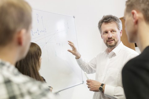 Professor an Whiteborad mit Studenten und Studentinnen um ihn herum