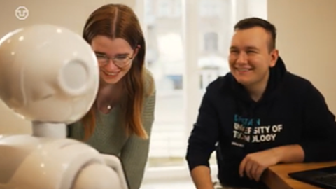 Zu sehen sind zwei Studierende, die mit einem Roboter interagieren