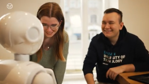 Zu sehen sind zwei Studierende, die mit einem Roboter interagieren