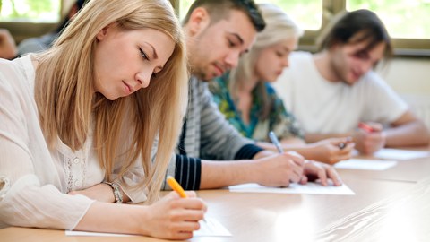 Foto von vier Studierenden, die nebeneinander an einem Tisch sitzen und etwas schreiben.