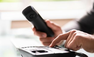 Foto einer Person, die eine Nummer in ein schwarzes Bürotelefon eingibt