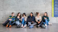 Foto von 6 Studierenden, die auf dem Boden eines TUD-Gebäudes sitzen und sich unterhalten.