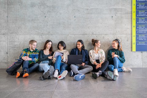 Foto von 6 Studierenden, die auf dem Boden eines TUD-Gebäudes sitzen und sich unterhalten.